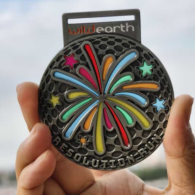 A hand holds a round "Resolution Run" medal featuring colorful fireworks and stars, with the "wildearth" logo at the top—an eye-catching piece of custom merchandise perfect for showcasing unique promotional products.